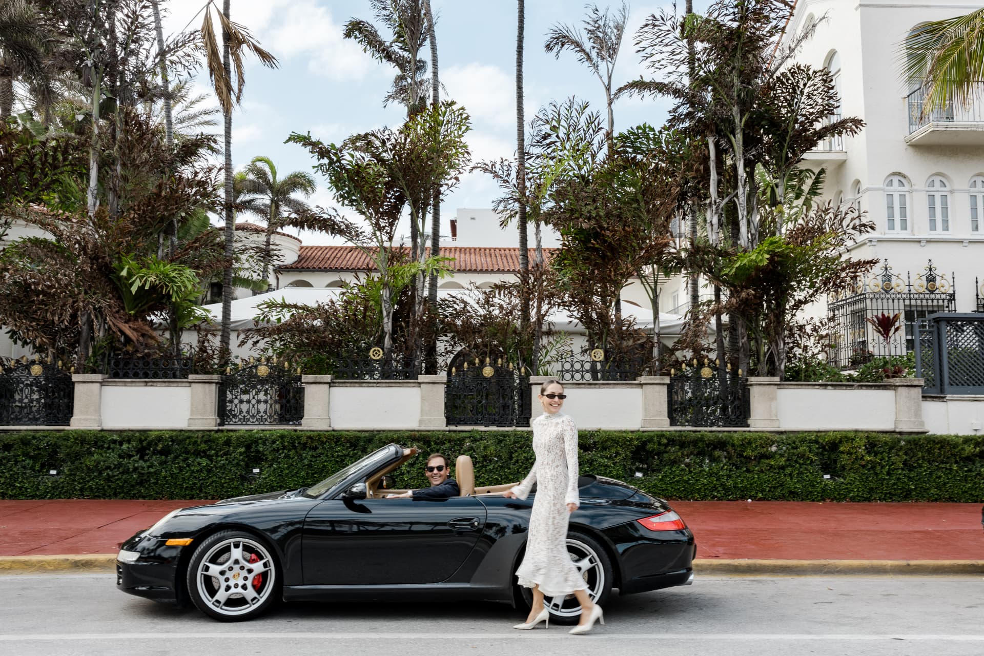 The couple with a black convertible on a palm-lined street